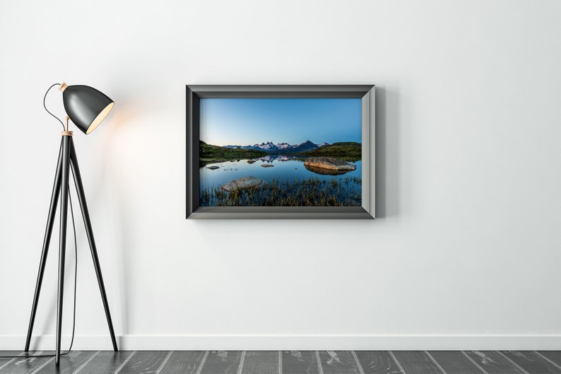 May include: A framed photograph of a mountain range reflected in a still lake. The mountains are snow-capped and the lake is a deep blue. The photo is in a black frame.