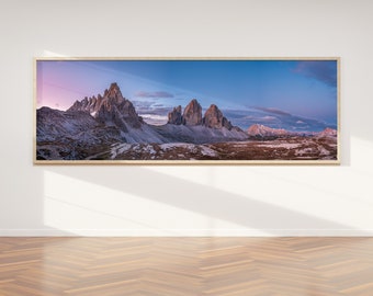 May include: A panoramic photograph of a mountain range with a pink and blue sky in the background. The mountains are rocky and jagged, and the sky is filled with clouds. The photo is framed in a wooden frame.