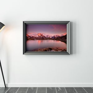 May include: A framed photograph of a mountain lake with snow-capped peaks reflecting in the water at sunset. The sky is a vibrant purple and pink.