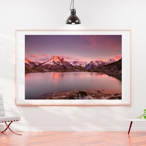 May include: A framed photograph of a mountain lake with snow-capped mountains reflecting in the water at sunset. The sky is a vibrant pink and purple.