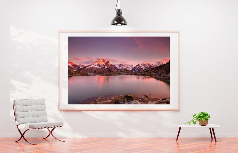 May include: A framed photograph of a mountain lake with snow-capped mountains reflecting in the water at sunset. The sky is a vibrant pink and purple.