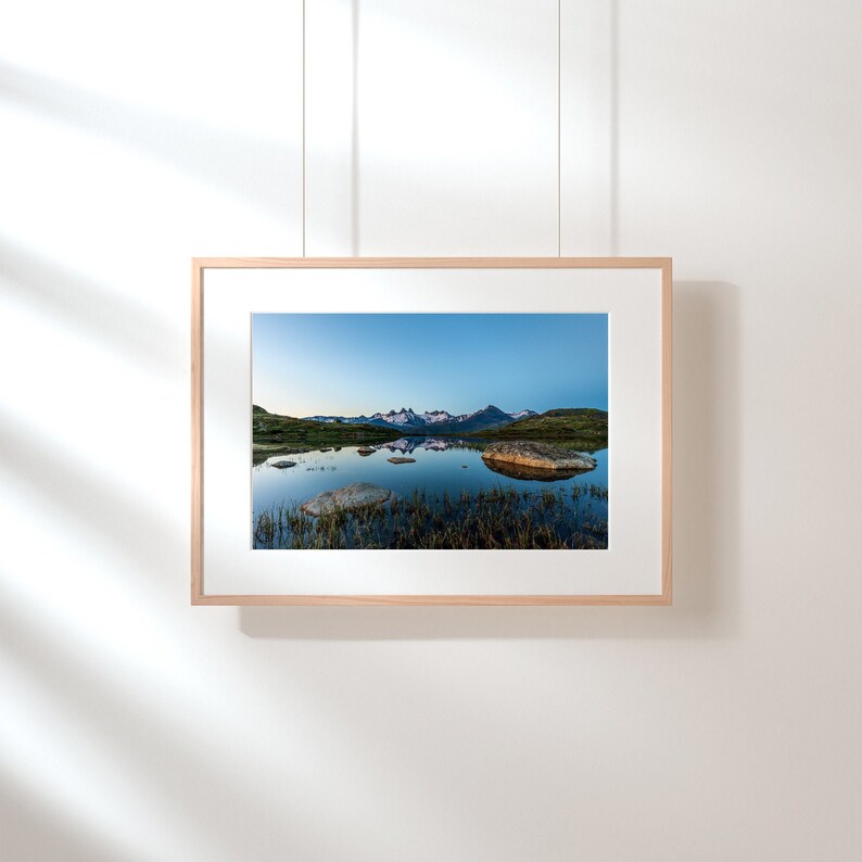 May include: A framed photograph of a mountain lake reflecting the surrounding peaks. The water is still and the sky is a light blue.