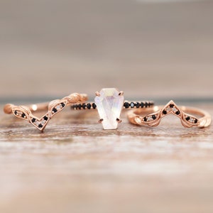 May include: Three rose gold rings with black and white diamonds. The center ring features a large, clear, faceted gemstone.