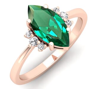 May include: A marquise cut emerald gemstone ring set in rose gold with a halo of smaller diamonds.