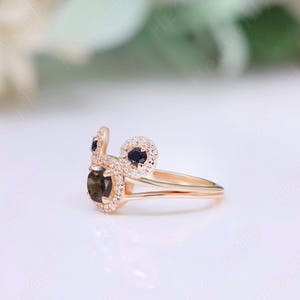 May include: A gold ring with a brown gemstone surrounded by smaller white gemstones. The ring has two smaller black gemstones on either side of the larger gemstone.