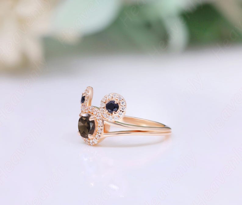 May include: A gold ring with a brown gemstone surrounded by smaller white gemstones. The ring has two smaller black gemstones on either side of the larger gemstone.