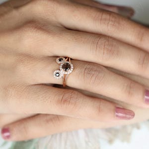 May include: A rose gold ring with three round brown diamonds set in a halo of smaller white diamonds.