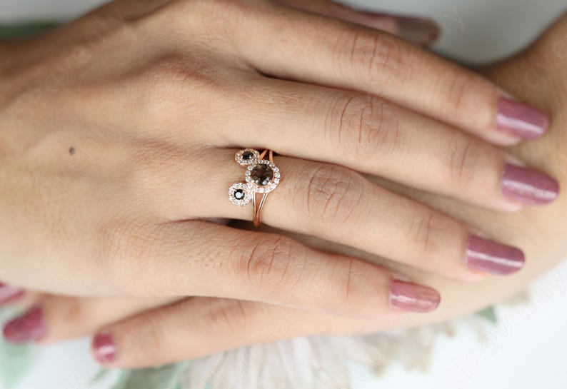 May include: A rose gold ring with three round brown diamonds set in a halo of smaller white diamonds.