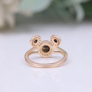 May include: A gold ring with three round stones. The center stone is larger than the two smaller stones on either side. The ring is set with small diamonds around the stones.