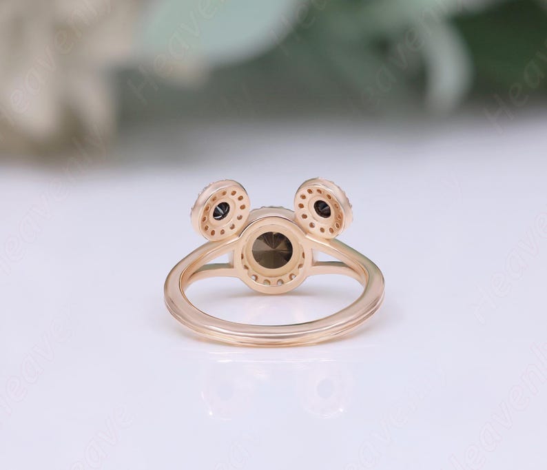 May include: A gold ring with three round stones. The center stone is larger than the two smaller stones on either side. The ring is set with small diamonds around the stones.