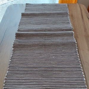 Op de afbeelding: Een bruin geweven placemat met een textuur. De placemat is gemaakt van dunne stroken materiaal die aan elkaar zijn geweven.