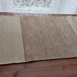 Peut inclure: Un chemin de table tiss&eacute; compos&eacute; de trois sections. La section centrale est de couleur brun fonc&eacute;, tandis que les deux sections ext&eacute;rieures sont de couleur beige clair.