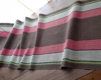 May include: A brown, pink, white and green striped fabric with a textured weave. The fabric is folded and draped over a wooden surface.