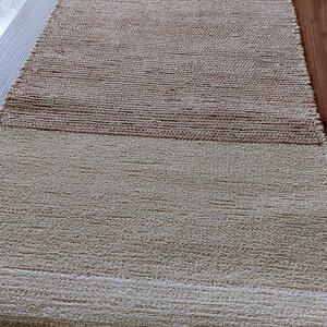 Peut inclure: Un tapis tiss&eacute; de couleur beige naturel avec une bande brune au milieu. Le tapis a une frange sur le bord inf&eacute;rieur.
