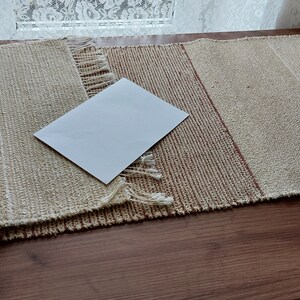 Peut inclure: Un chemin de table tiss&eacute; beige et brun avec une carte blanche sur le dessus. Le chemin de table a une bordure frang&eacute;e.