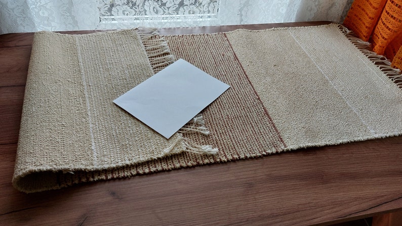 Peut inclure: Un chemin de table tiss&eacute; beige et brun avec une carte blanche sur le dessus. Le chemin de table a une bordure frang&eacute;e.