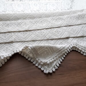May include: White crocheted lace valance with a scalloped edge and a fringe trim. The valance is folded in thirds and has a delicate pattern.