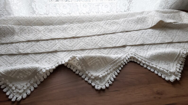 May include: White crocheted lace valance with a scalloped edge and a fringe trim. The valance is folded in thirds and has a delicate pattern.