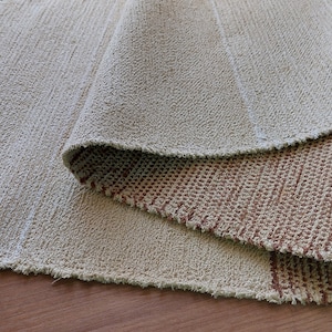Peut inclure: Un tapis tiss&eacute; beige et brun avec des franges sur les bords. Le tapis est pli&eacute; en deux, r&eacute;v&eacute;lant le motif tiss&eacute; brun en dessous.