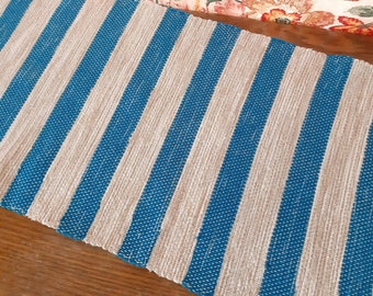May include: A blue and beige striped rug with a woven texture. The rug is made of natural fibers and has a simple, modern design.