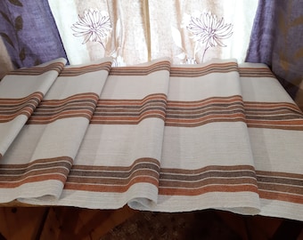 May include: A folded linen table runner with brown and orange stripes. The runner is folded in thirds and has a natural linen texture.