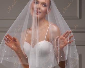 May include: A bride wearing a white satin wedding dress with a sweetheart neckline and spaghetti straps. A sheer veil, adorned with scattered pearls, drapes over the bride's head and shoulders. The veil is embellished with the text "Maria Bride".