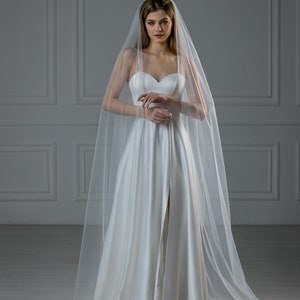 K&ouml;nnte beinhalten: Eine Braut in einem wei&szlig;en Brautkleid mit langem Schleier. Das Kleid hat einen herzf&ouml;rmigen Ausschnitt und einen Schlitz vorne.