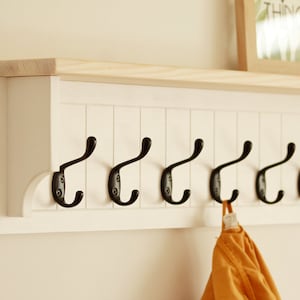 May include: White wooden coat rack with a shelf on top and eight black metal hooks. A yellow garment is hanging on one of the hooks.