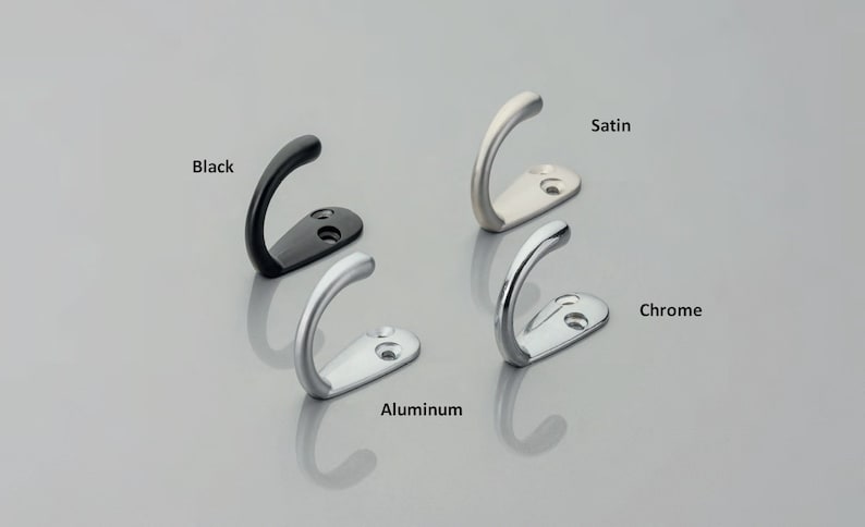 May include: Four metal wall hooks with curved designs and two screw holes on the base. The finishes are labeled as Black, Satin, Aluminum, and Chrome. Each hook features a smooth, rounded top and a flat mounting plate for secure installation.