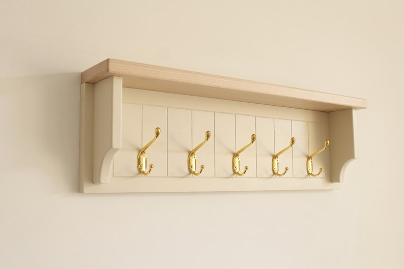 May include: A cream-colored wooden coat rack with five gold hooks and a top shelf.
