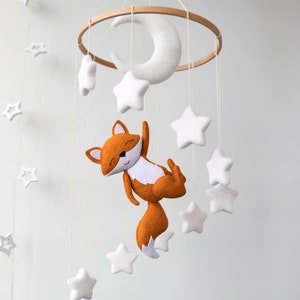 May include: A white felt crescent moon and white felt stars hang from a wooden ring, with a felt orange fox hanging from the bottom.