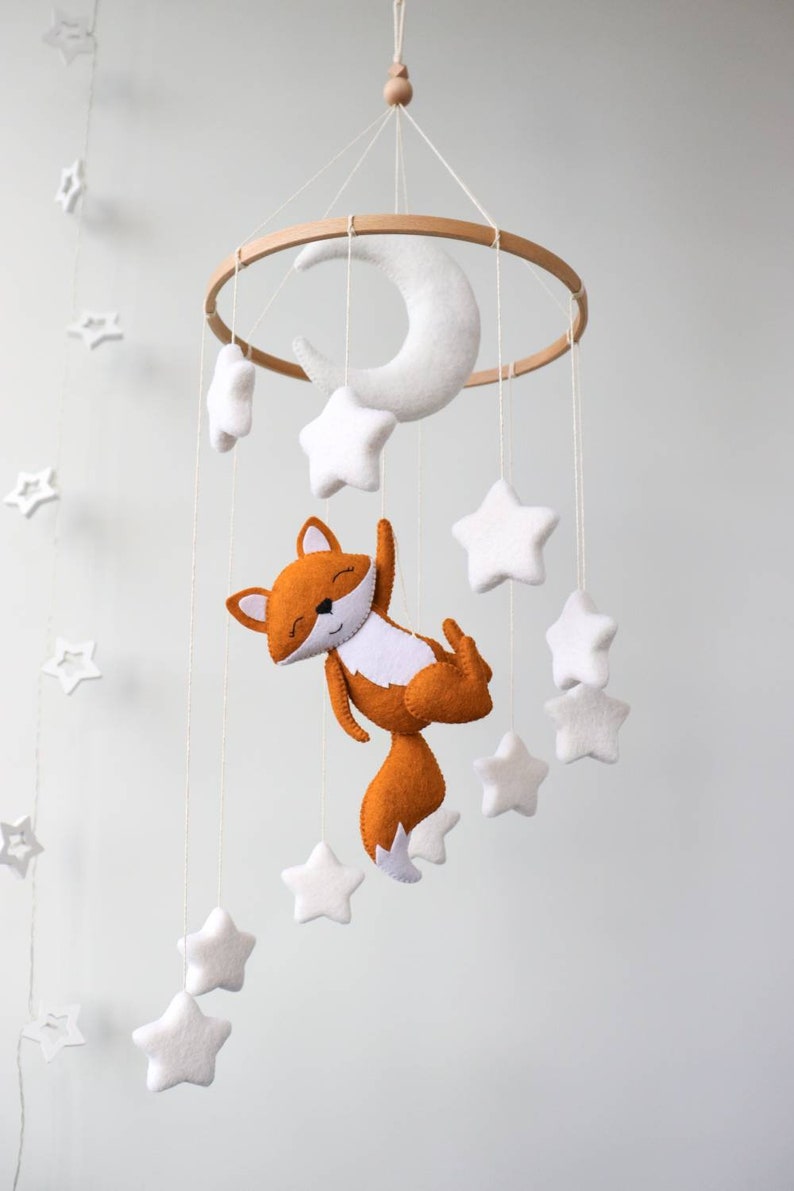May include: A white felt crescent moon and white felt stars hang from a wooden ring, with a felt orange fox hanging from the bottom.
