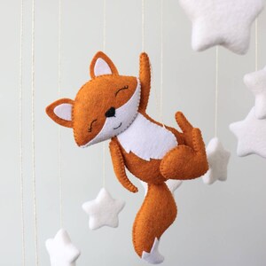May include: A white felt moon and stars mobile with a brown felt fox hanging from it. The fox has a white belly and a white tip on its tail.