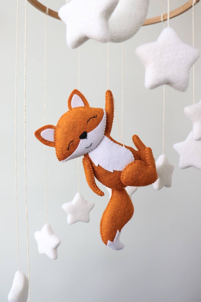 May include: A white felt moon and stars mobile with a brown felt fox hanging from it. The fox has a white belly and a white tip on its tail.
