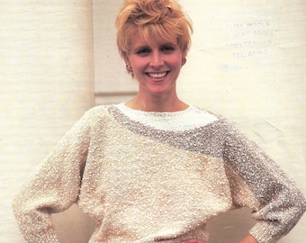 May include: A woman with short blonde hair is wearing a beige sweater with a white trim and white pants. The sweater is knit with a textured yarn. The image is from a 1993 knitting pattern book by Richard Poppleton for Plaza DK yarn.
