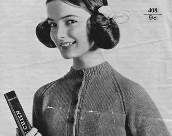 May include: A black and white photo of a woman wearing a knitted cardigan with a button-up front. The cardigan is labeled "GREENOCK double knitting or BRY-NYLON quick-knit".