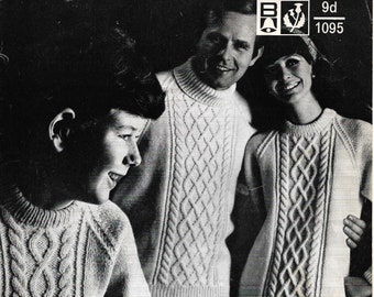 May include: A black and white photo of three people wearing white cable knit sweaters. The sweaters have a vertical cable knit pattern. The photo is from a knitting pattern book. The text on the page reads "Aran knitting Sizes 26 to 44".