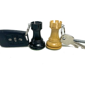 May include: A black and a natural wood chess rook keychain with a silver key ring. The key ring is attached to a black car key fob.