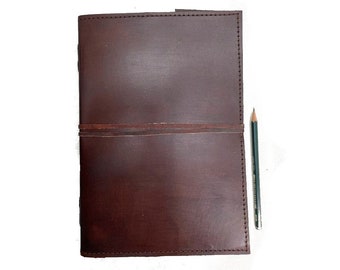 May include: A brown leather journal with a stitched edge and a leather strap closure. A pencil is lying next to the journal.