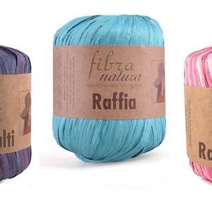 May include: Three spools of raffia yarn in shades of purple, teal, and pink. Each spool has a brown paper label with the text "fibra natura" and "Raffia Multi". The yarn is made of natural fibers and is suitable for crafting.