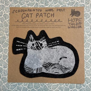 May include: A screen-printed wool felt cat patch on a brown card. The patch features a stylized grey cat design with a black border. Text on the card reads "CAT PATCH" and "HOPE TALBOT WALLER."