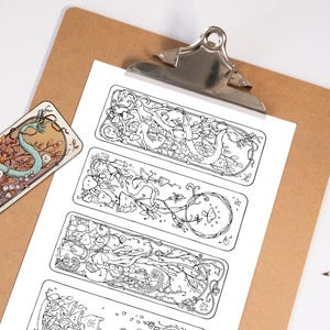 May include: A selection of illustrated bookmarks and designs. The bookmarks feature detailed black and white line art of fantastical creatures and nature elements. Pencils and a clipboard are also visible.