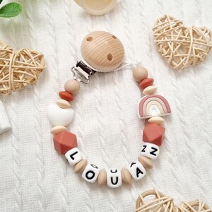 Attache tétine personnalisée arc en ciel pour bébé avec des perles silicone beige et terracotta, une perle motif coeur.