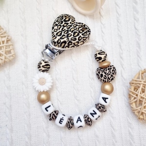 Può includere: Un portaciuccio con una perla a forma di cuore con stampa leopardata, una clip in metallo e una serie di perline in stampa leopardata, oro e bianco. Le perline bianche compongono il nome LEANA in lettere nere, con una perla a margherita.