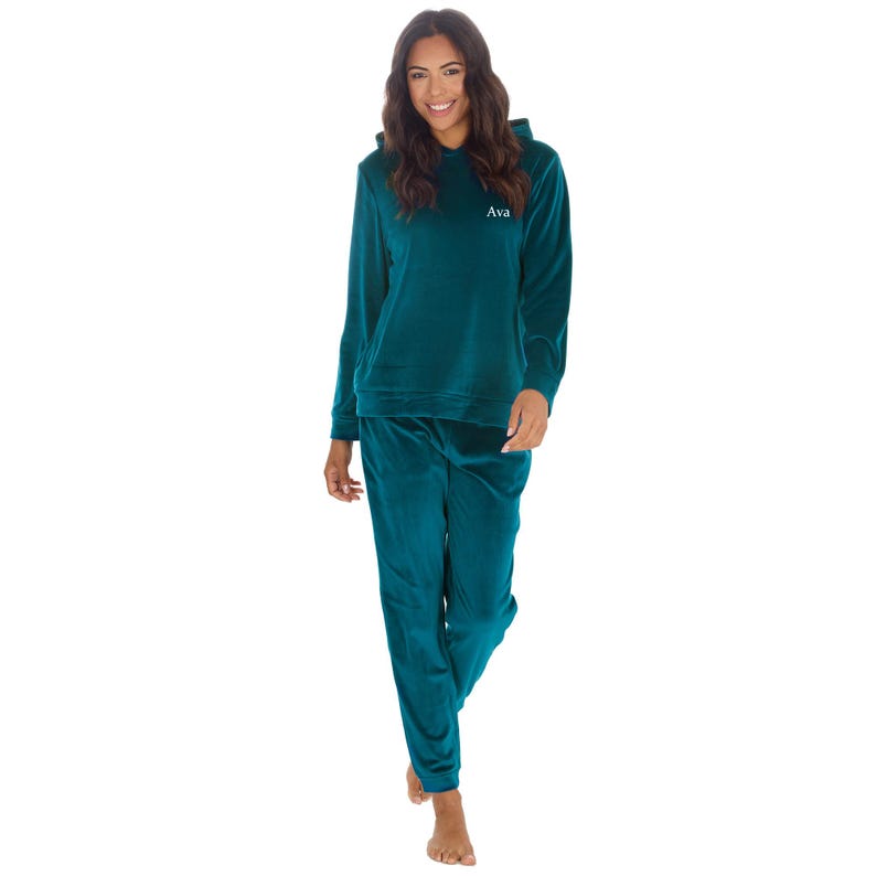 May include: A teal blue velour hooded sweatshirt and matching sweatpants set. The sweatshirt has a drawstring hood and the text "Ava" embroidered on the front.