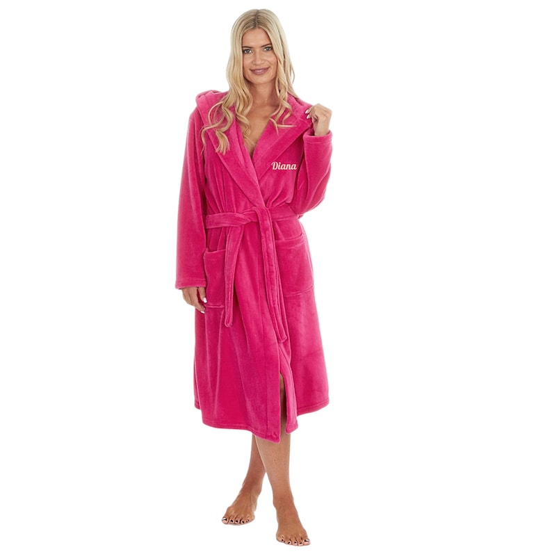 May include: A vibrant pink hooded robe with the name "Diana" embroidered on the chest. The robe features a matching belt, pockets, and a soft, plush texture. This cozy garment is designed for comfort and relaxation.