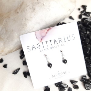 May include: Sagittarius black obsidian earrings on a white card with the text "Sagittarius Black Obsidian" and "Alcyone - Dream & Wish".