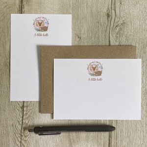 May include: Two white note cards with a brown envelope. The note cards feature a cute cartoon illustration of a deer with a floral wreath around it. The text "A little hello" is printed on both cards.