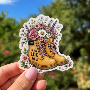 May include: A sticker featuring a pair of yellow work boots filled with a bouquet of flowers. The boots have pink laces and the text "in my LDC era". The flowers include pink roses, daisies, and lavender.