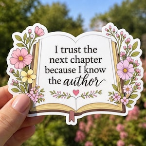 May include: A sticker in the shape of an open book, with the text "I trust the next chapter because I know the author." The sticker is decorated with pink and yellow flowers and green leaves.